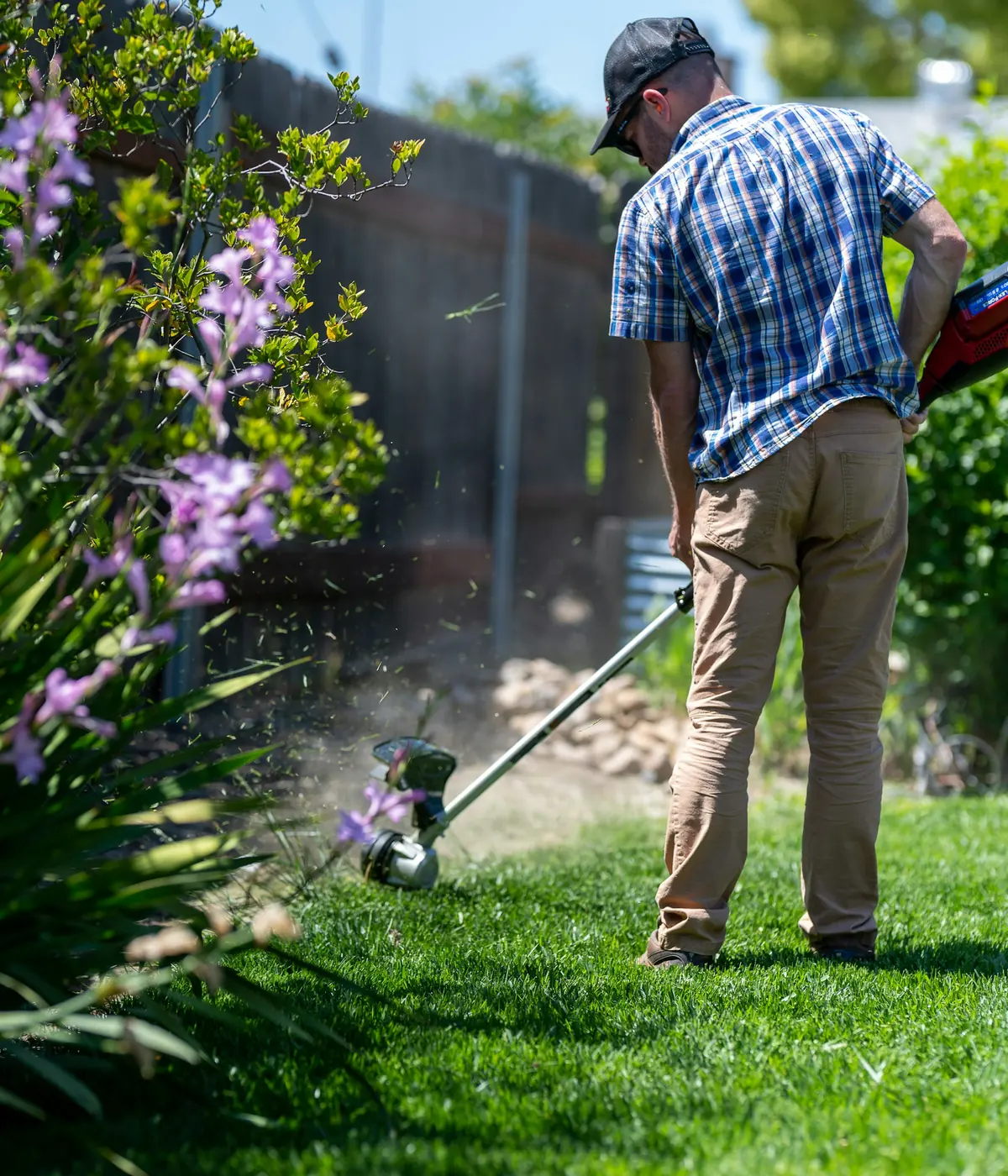 Grounds maintenance worker edging a neat residential lawn beside a planted garden border